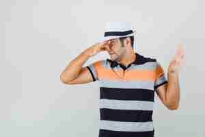 Free photo young man holding his nose while showing reject gesture in t-shirt,hat and looking disgusted.