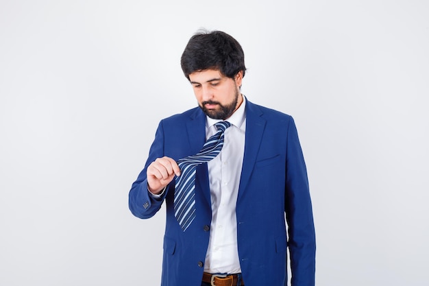 Young man holding his tie in shirt,jacket,tie and looking focused , front view.