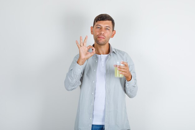 Молодой человек, держащий стакан сока с хорошо знаком в рубашке