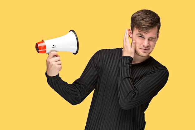 young man holding a megaphone on on yellow studio background