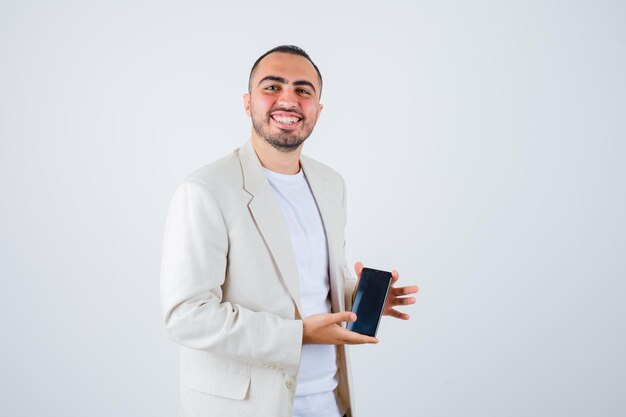 Young man holding mobilephone in white t-shirt, jacket and looking happy , front view.