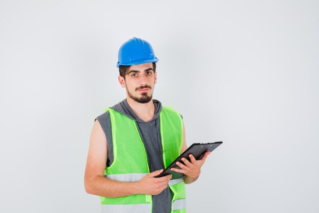 Young man holding notebook in construction uniform and looking happy