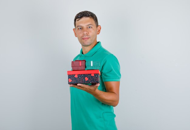 Young man holding paper bags in green t-shirt and looking confident, front view.