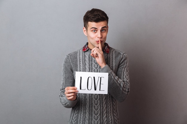 Young man holding paper with love text showing silence gesture.