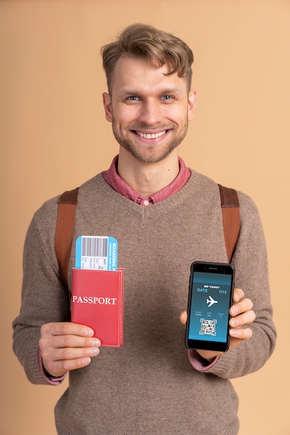 Free photo young man holding passport with plane tickets and smartphone