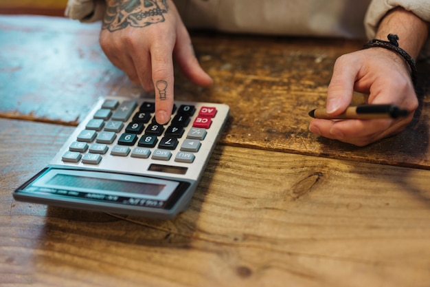 Young man holding pen using calculator in his shop