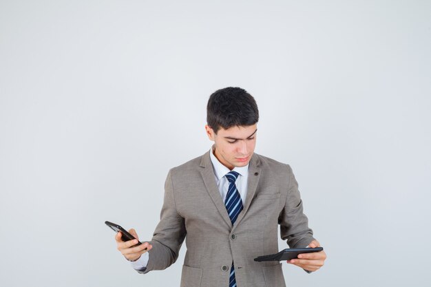 Young man holding phone, looking at calculator in formal suit