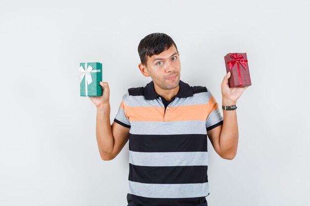 Young man holding present boxes in t-shirt and looking cheerful 