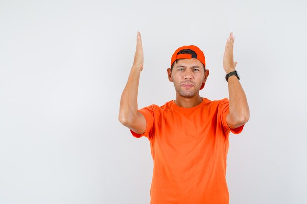 Young man holding raised arms even in orange t-shirt and cap front view.