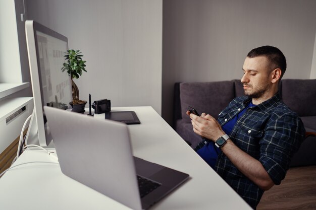 Young man holding smartphone in hands while making a pause in home office