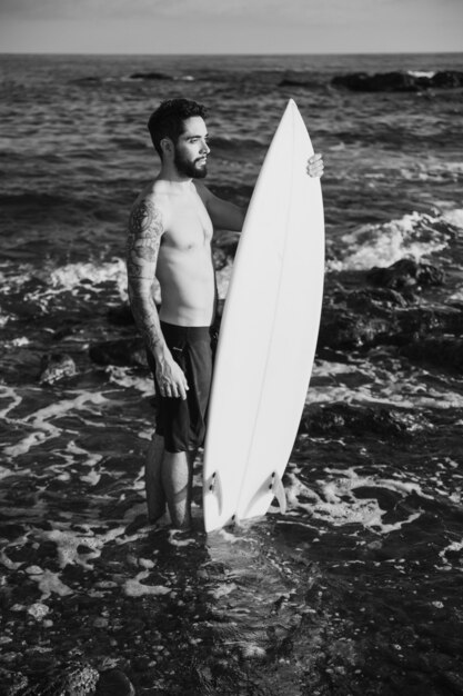 Young man holding surf board in water 