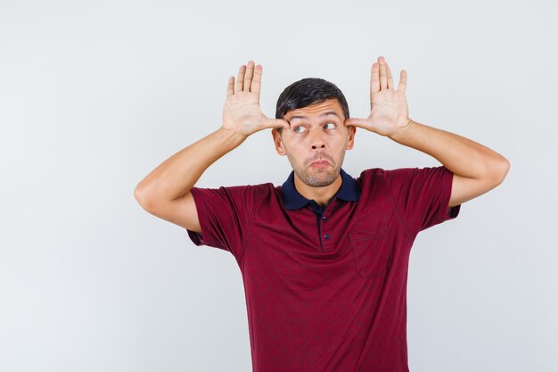 Young man holding thumbs on temples while imitating ears in t-shirt and looking funny. front view.