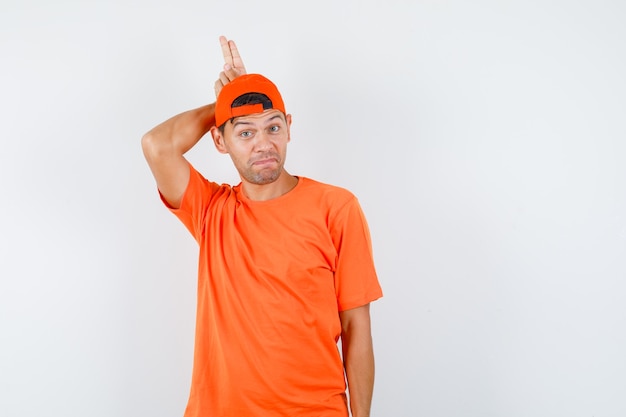 주황색 티셔츠와 모자에 뿔처럼 머리 뒤에 두 손가락을 들고 웃기는 젊은 남자