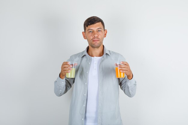 Young man holding two glasses of juice in shirt front view.