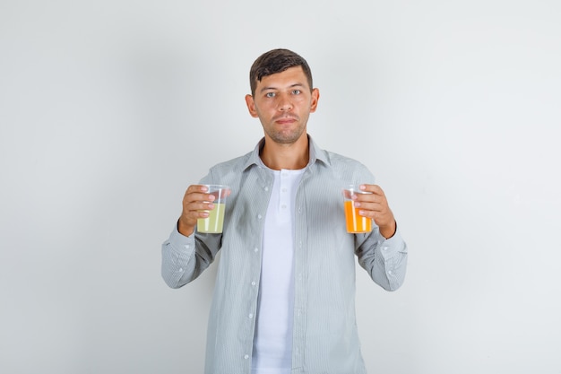 Молодой человек, держащий два стакана сока в вид спереди рубашку.