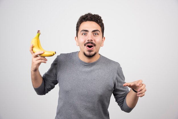 Young man holding two ripe bananas on gray.