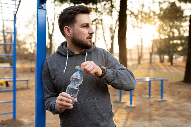 運動公園で屋外で水のボトルを保持している若い男