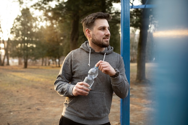 運動公園で屋外で水のボトルを保持している若い男
