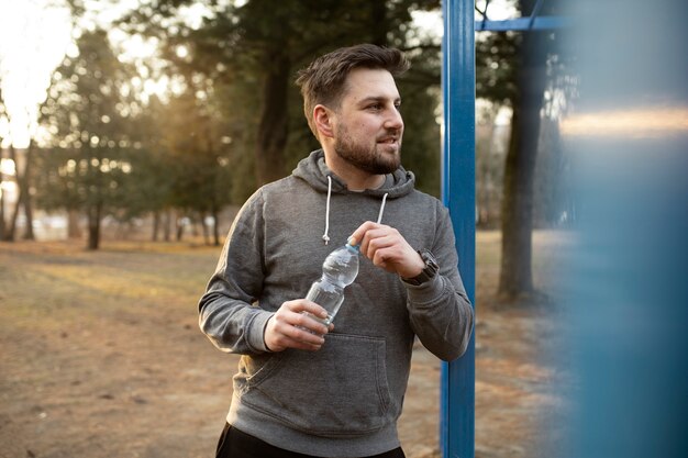 young man holding water bottle outdoors while at exercise park