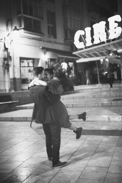 Young man holding and whirling with laughing woman on street 