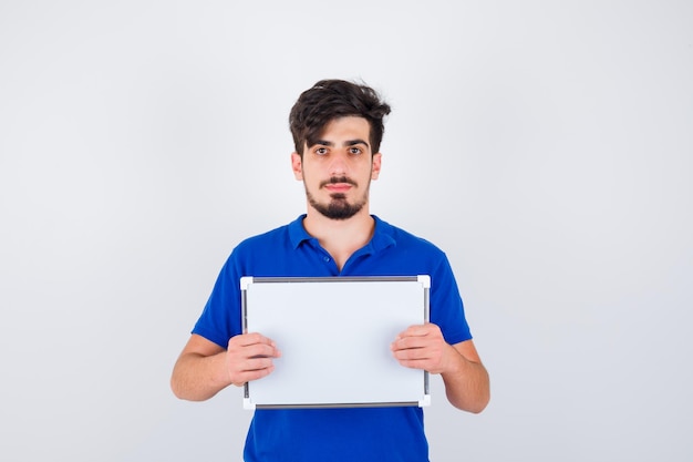 Young man holding whiteboard in blue t-shirt and looking serious