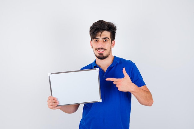 Young man holding whiteboard and pointing to it in blue t-shirt and looking happy