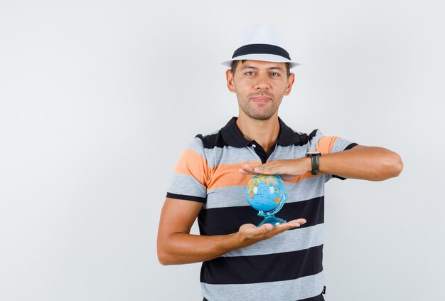 Young man holding world globe in t-shirt and hat and looking careful