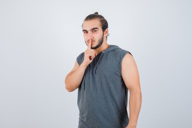 Young man in hooded t-shirt showing silence gesture and looking serious , front view.