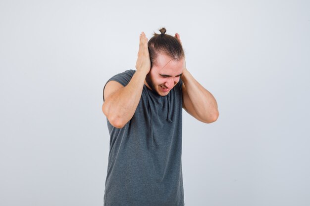 Young man in hoodie covering ears with palms and looking dissatisfied , front view.