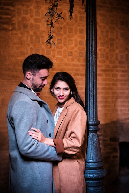 Young man hugging attractive happy woman near street lamp