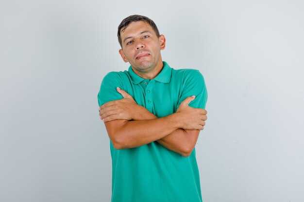 Young man hugging himself in green t-shirt, front view.