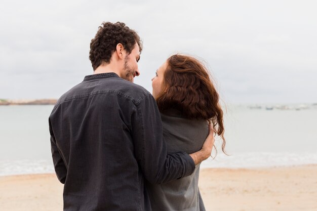 Young man hugging woman in blanket on sea shore 