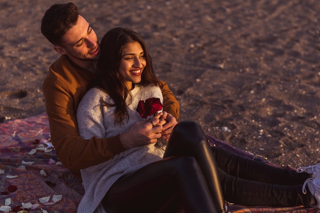 Foto gratuita giovane che abbraccia la donna sul coverlet sulla riva di mare