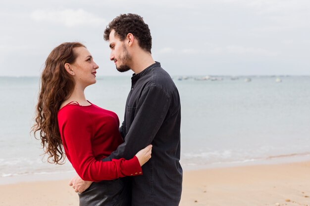 Young man hugging woman on sandy sea shore 