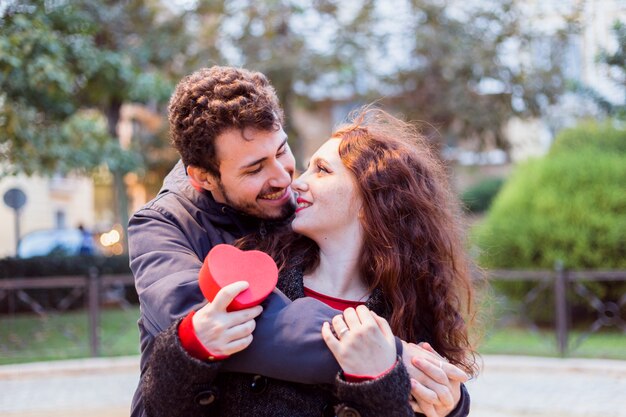 Young man hugging woman with gift box from behind 