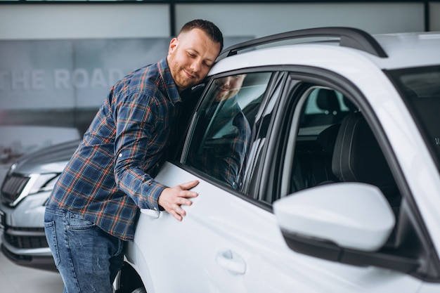 Young man huggingf a car in a car showroom