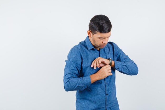 Бесплатное фото Молодой человек в синей рубашке носить часы и смотрит осторожно, вид спереди.