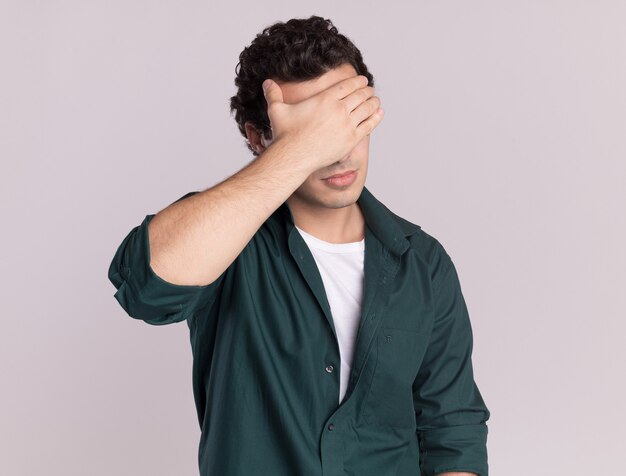 무료 사진 녹색 셔츠에 젊은 남자가 피곤하고 흰 벽 위에 서있는 손으로 눈을 감고 지루