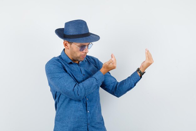 Young man inviting to come in blue shirt, hat and looking confident. front view.