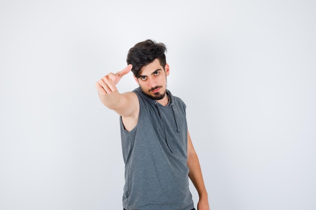 Young man inviting to come in gray shirt and looking serious