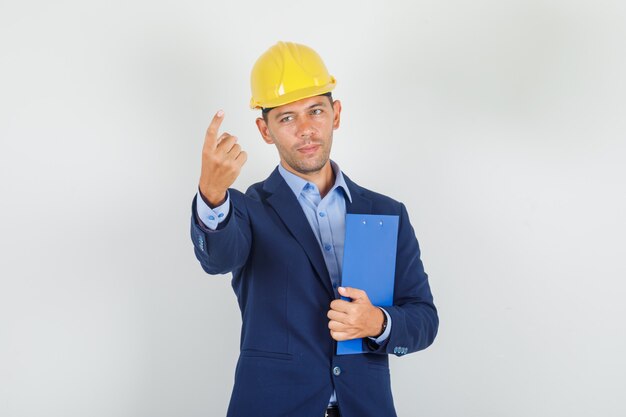 Young man inviting to come with finger in suit, safety helmet