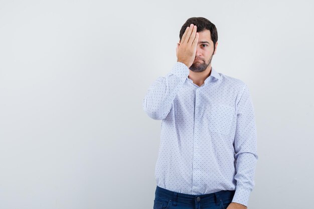 The young man is covering half-face with hand on white background