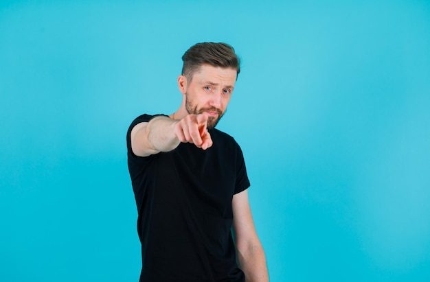 Young man is extending forefinger to camera on blue background