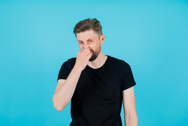 Young man is holding nose on blue background
