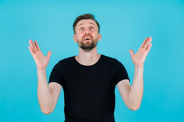 Young man is looking up by raising up his hands on blue background