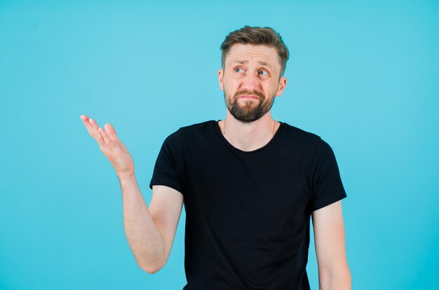 Young man is looking up and pointing up with hand on blue background