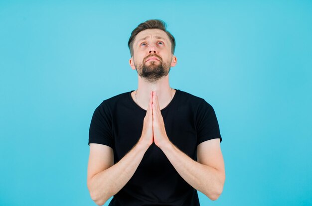 Young man is looking up and praying by holding hands together on blue background