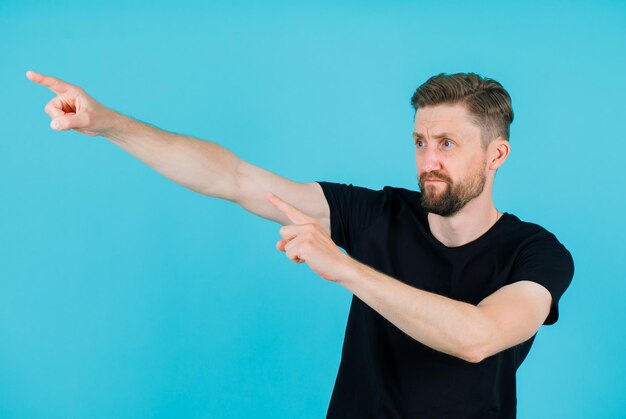 Young man is pointing away with forefingers on blue background