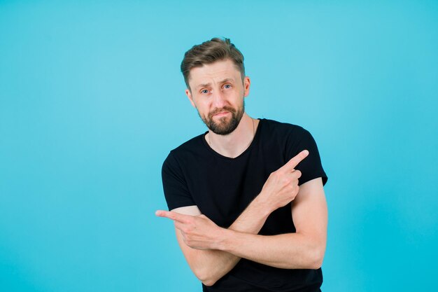 Young man is pointing right and left by crossing hands on blue background