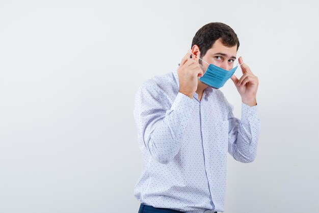 The young man is putting on medical mask on white background